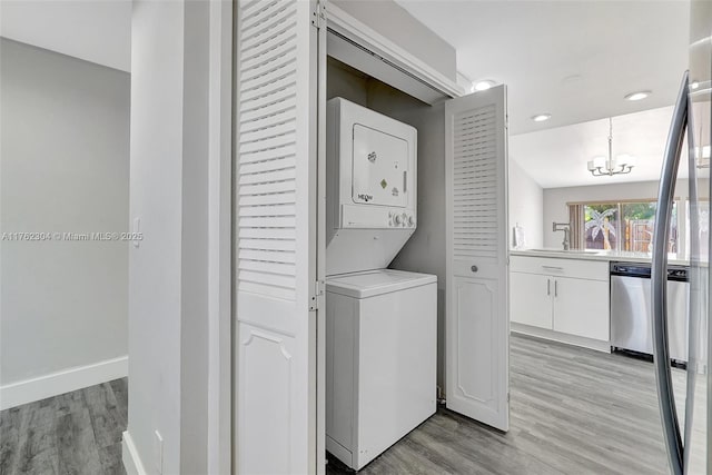 clothes washing area featuring light wood-style floors, stacked washer and clothes dryer, laundry area, and an inviting chandelier