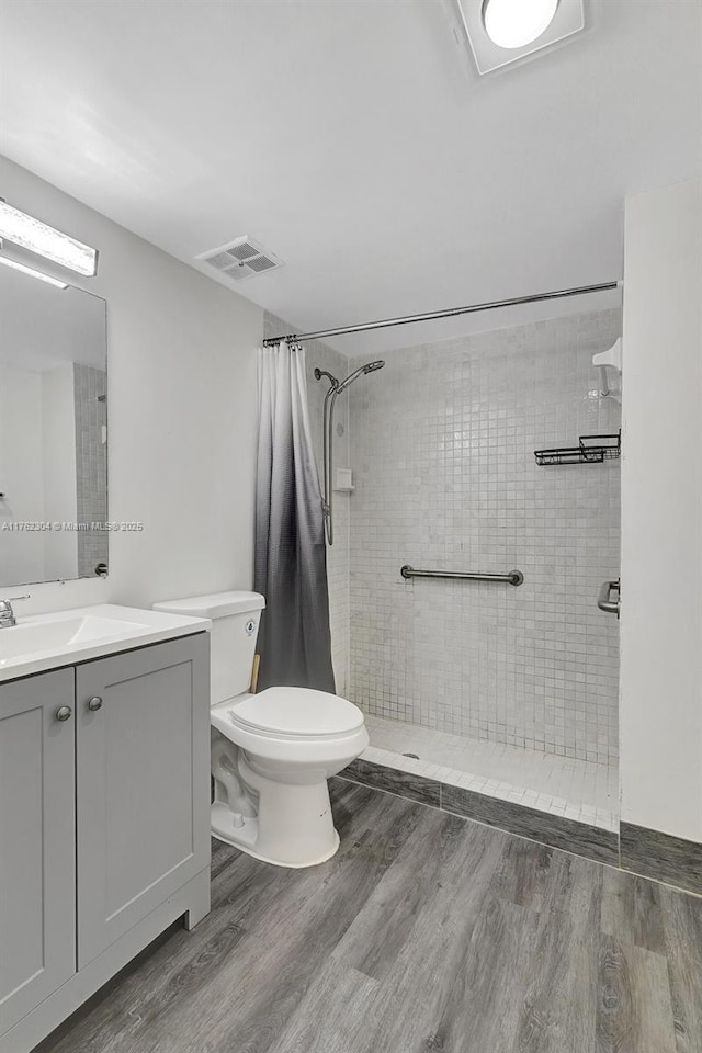 full bath featuring visible vents, toilet, wood finished floors, tiled shower, and vanity