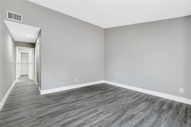 spare room featuring visible vents, baseboards, and dark wood finished floors