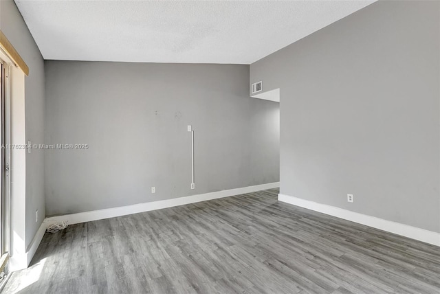 empty room featuring visible vents, baseboards, lofted ceiling, wood finished floors, and a textured ceiling