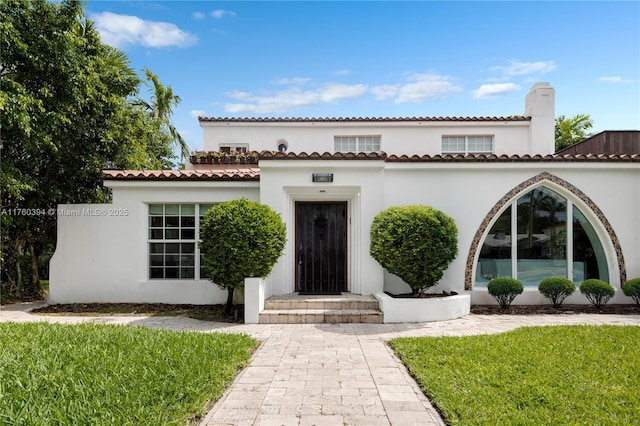 mediterranean / spanish home featuring stucco siding, a chimney, and a front lawn