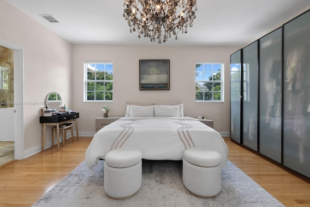 bedroom featuring light wood-type flooring, visible vents, a notable chandelier, ensuite bathroom, and baseboards