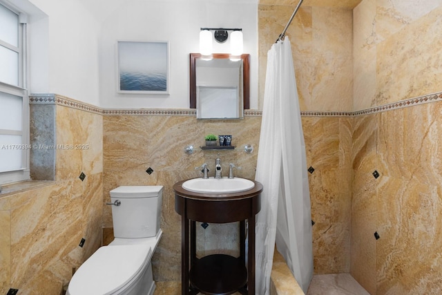 bathroom with wainscoting, tiled shower, toilet, and tile walls