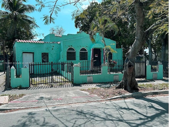 view of front facade featuring a tiled roof, a fenced front yard, a gate, and stucco siding