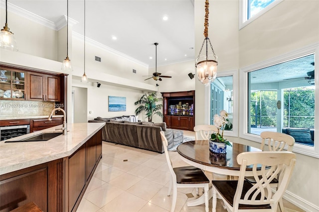 kitchen featuring light tile patterned floors, a ceiling fan, ornamental molding, a sink, and a towering ceiling