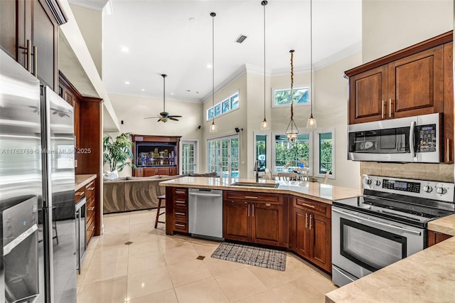 kitchen with light tile patterned floors, ornamental molding, appliances with stainless steel finishes, decorative light fixtures, and open floor plan