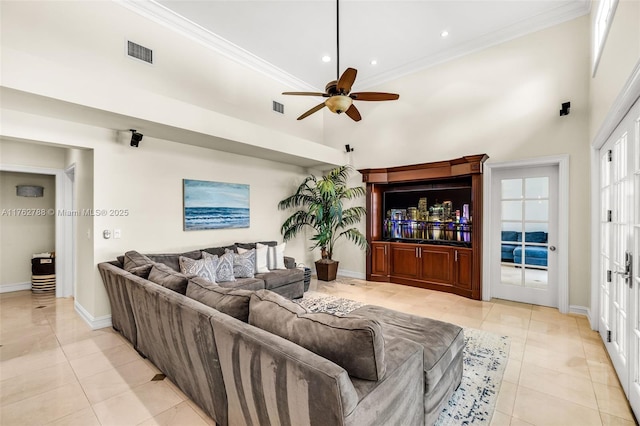 living area with ceiling fan, visible vents, a high ceiling, and ornamental molding