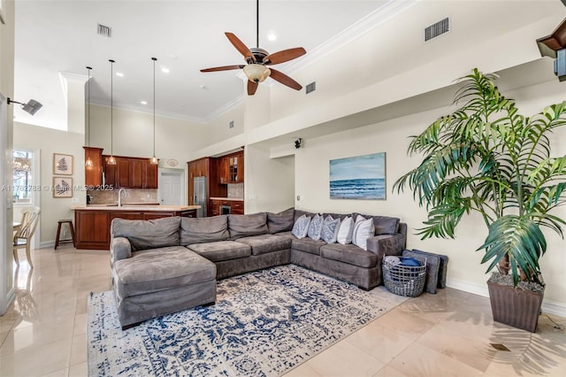 living area featuring visible vents, a towering ceiling, a ceiling fan, and crown molding