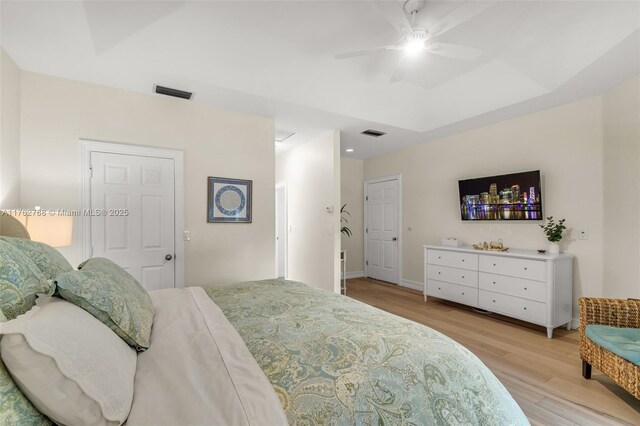 bedroom with ceiling fan, visible vents, light wood-style flooring, and a tray ceiling