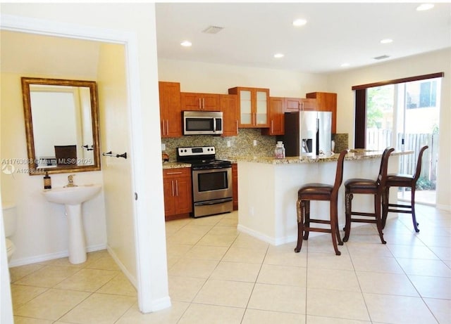 kitchen with tasteful backsplash, glass insert cabinets, a kitchen breakfast bar, light tile patterned flooring, and stainless steel appliances