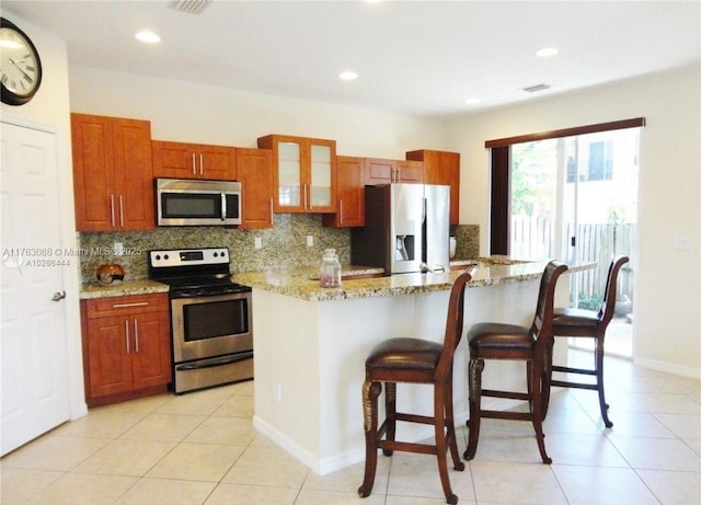 kitchen featuring decorative backsplash, brown cabinets, a kitchen bar, and stainless steel appliances