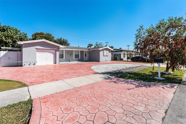 ranch-style home featuring decorative driveway, stucco siding, an attached garage, and fence