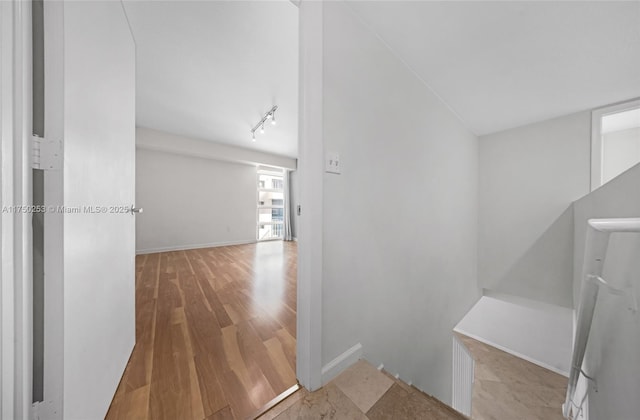 hallway featuring track lighting, wood finished floors, and baseboards