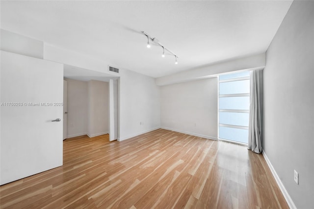 unfurnished room with visible vents, rail lighting, baseboards, and light wood-style floors