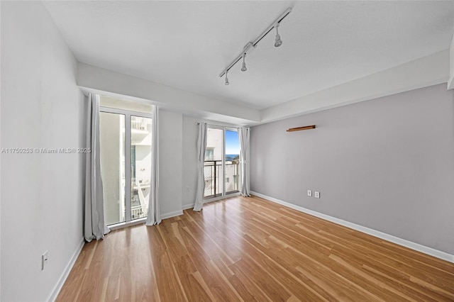 unfurnished room featuring track lighting, light wood-style flooring, and baseboards