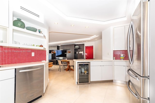 kitchen featuring a tray ceiling, stainless steel appliances, light countertops, wine cooler, and white cabinetry