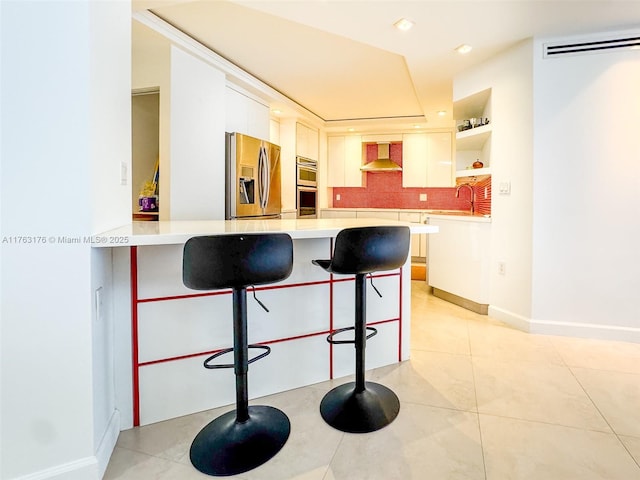 kitchen featuring light countertops, a breakfast bar area, appliances with stainless steel finishes, a peninsula, and wall chimney range hood