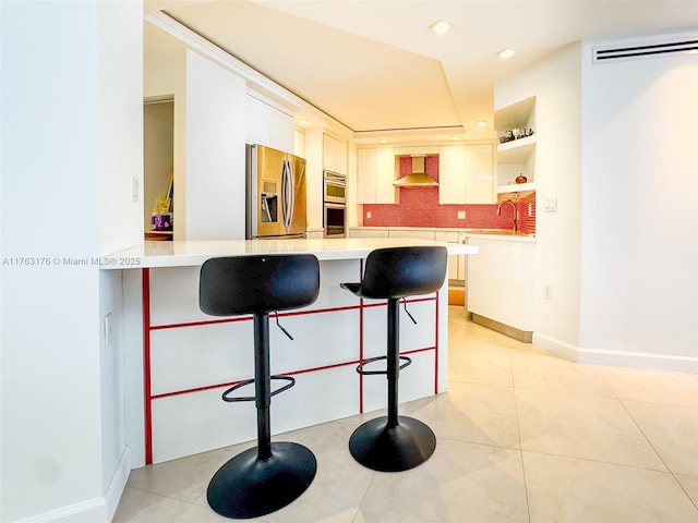 kitchen with wall chimney range hood, light countertops, a kitchen breakfast bar, appliances with stainless steel finishes, and a peninsula