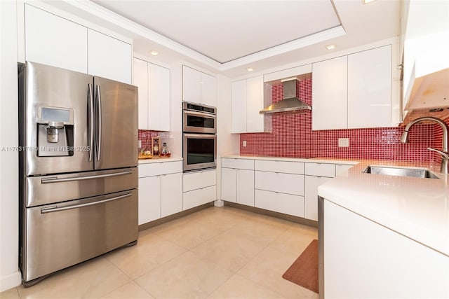 kitchen with light countertops, a sink, white cabinetry, stainless steel appliances, and wall chimney range hood