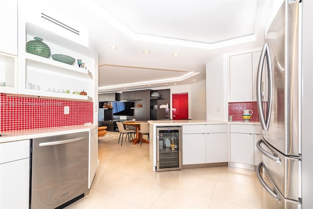 kitchen with light countertops, wine cooler, stainless steel appliances, a raised ceiling, and white cabinetry