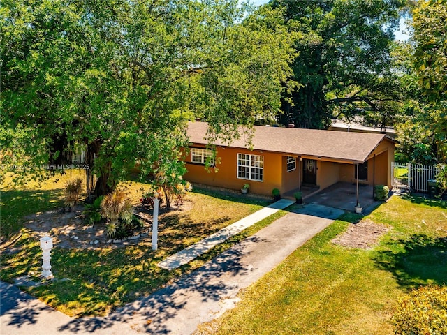 ranch-style home with stucco siding, driveway, fence, a front yard, and a carport