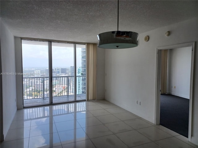 empty room featuring light tile patterned floors, a view of city, a textured ceiling, and a wall of windows