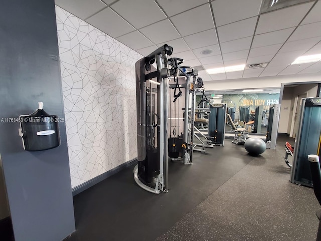 exercise room featuring a paneled ceiling, visible vents, and baseboards