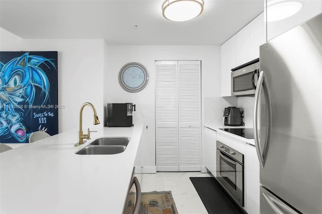 kitchen with a sink, stainless steel appliances, white cabinetry, and light countertops