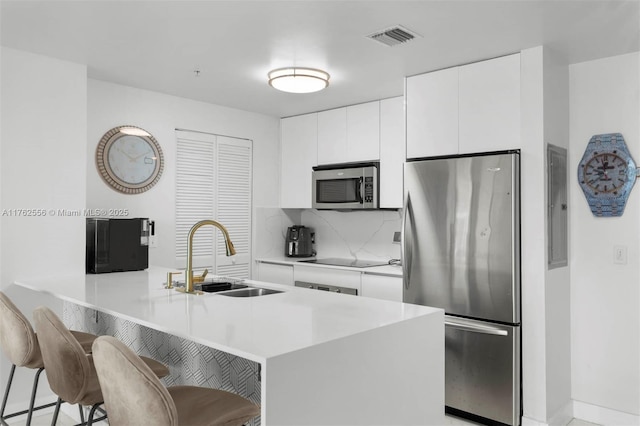 kitchen with visible vents, a peninsula, a sink, appliances with stainless steel finishes, and white cabinetry