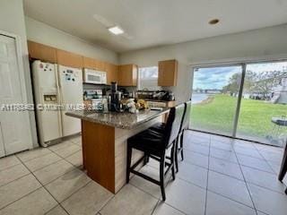 kitchen featuring dark countertops, a kitchen island, a breakfast bar area, light tile patterned floors, and white appliances