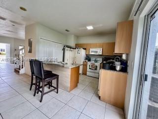 kitchen with a breakfast bar, white appliances, light tile patterned floors, and a peninsula