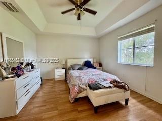 bedroom featuring a tray ceiling, visible vents, wood finished floors, and a ceiling fan