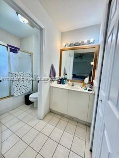 full bath with vanity, tile patterned floors, toilet, and combined bath / shower with glass door