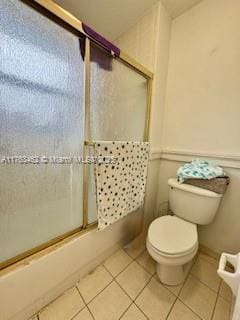 bathroom featuring tile patterned flooring, toilet, and bath / shower combo with glass door