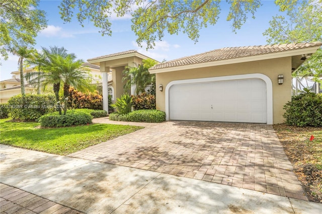 mediterranean / spanish house featuring stucco siding, an attached garage, a tile roof, and decorative driveway