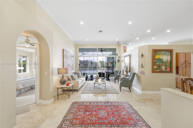 living area featuring arched walkways, a healthy amount of sunlight, ornamental molding, and a ceiling fan