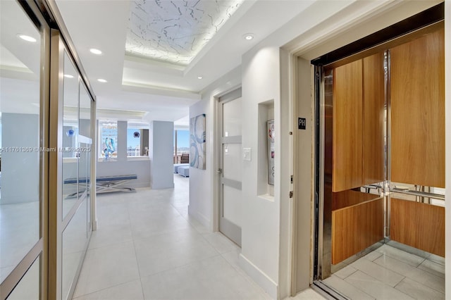hall featuring elevator, light tile patterned floors, recessed lighting, and a tray ceiling