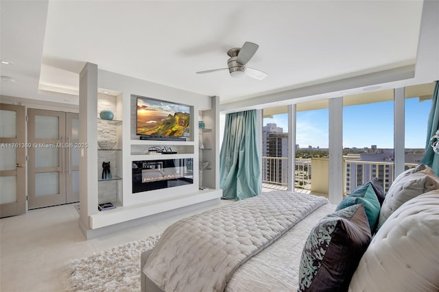 bedroom with access to exterior, floor to ceiling windows, light tile patterned floors, a glass covered fireplace, and a ceiling fan