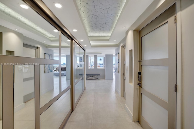 hallway featuring light tile patterned flooring, recessed lighting, a raised ceiling, and baseboards