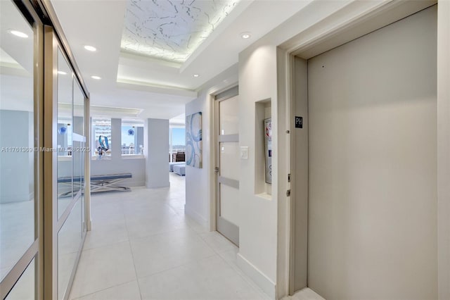 corridor featuring a tray ceiling, elevator, light tile patterned flooring, and recessed lighting