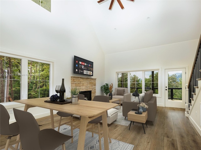 dining space featuring high vaulted ceiling, hardwood / wood-style flooring, a stone fireplace, ceiling fan, and stairs