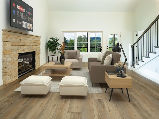 living area with wood finished floors, a stone fireplace, baseboards, a towering ceiling, and stairs