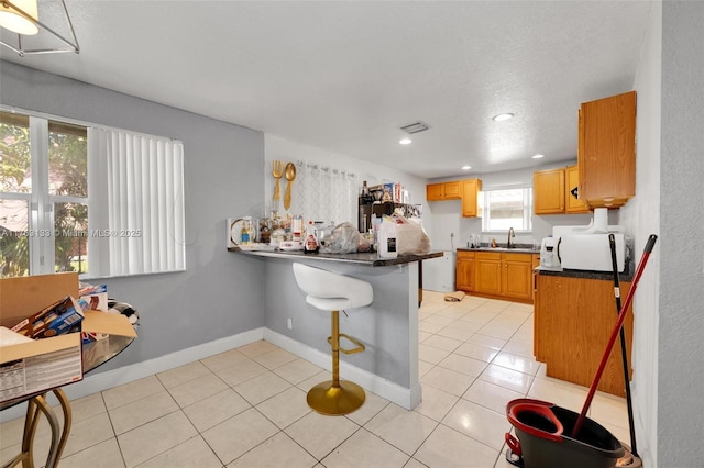 kitchen with light tile patterned floors, white microwave, a peninsula, a sink, and dark countertops