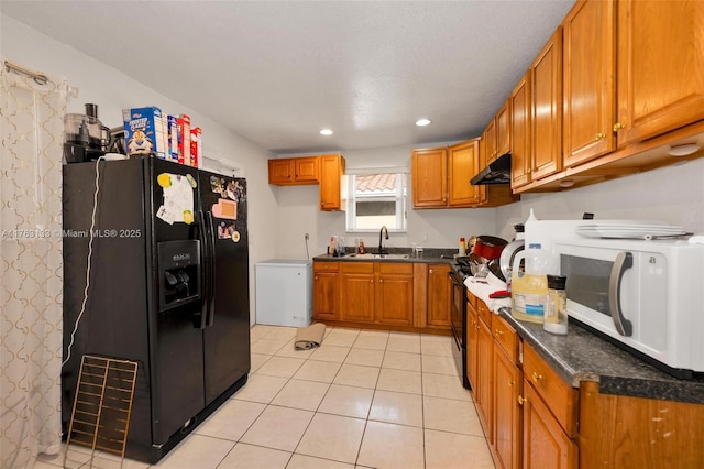 kitchen with brown cabinets, black appliances, under cabinet range hood, a sink, and light tile patterned floors