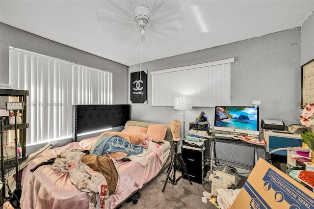 bedroom featuring a ceiling fan, a textured wall, and carpet floors