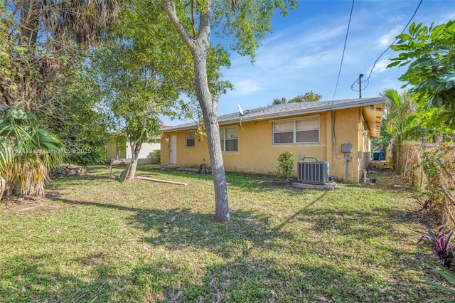 back of property with stucco siding, central air condition unit, a lawn, and fence