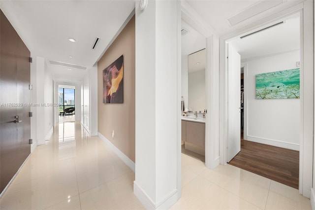 corridor with light tile patterned floors, visible vents, baseboards, and a sink