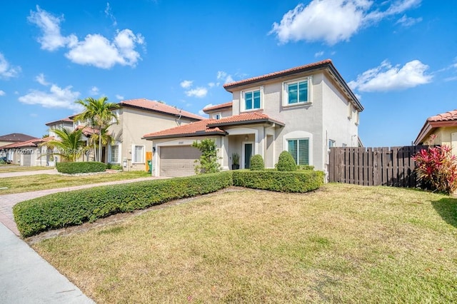 mediterranean / spanish-style home featuring stucco siding, driveway, a tile roof, a front lawn, and fence