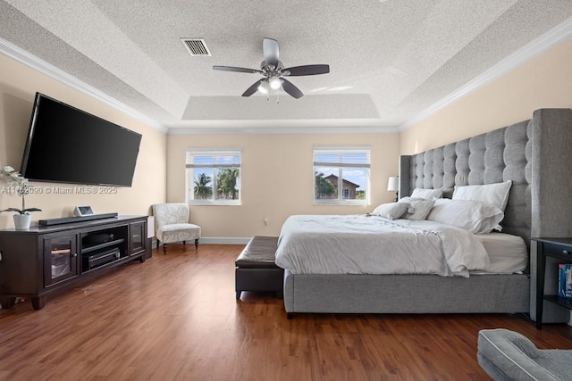 bedroom with a tray ceiling, wood finished floors, visible vents, and a textured ceiling