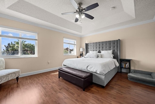 bedroom featuring a raised ceiling, a textured ceiling, wood finished floors, crown molding, and baseboards